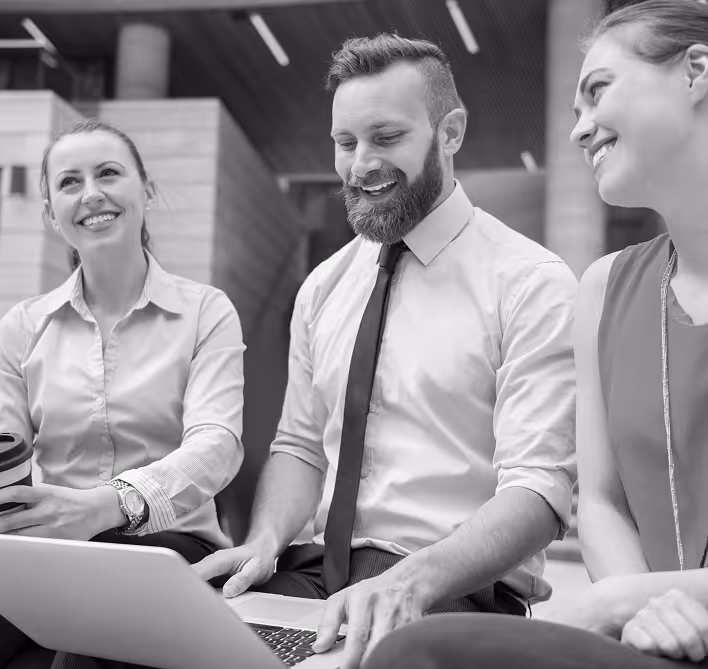 Three colleagues smiling and looking at a laptop during a casual office discussion.