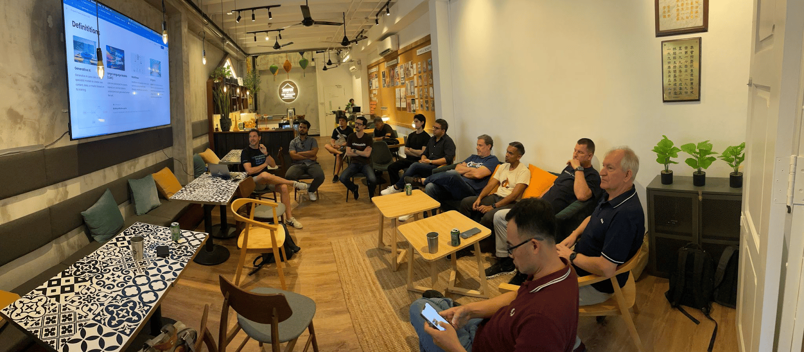 MISSION+ meetup in Singapore: engineers seated around a café listening to a talk on generative AI
