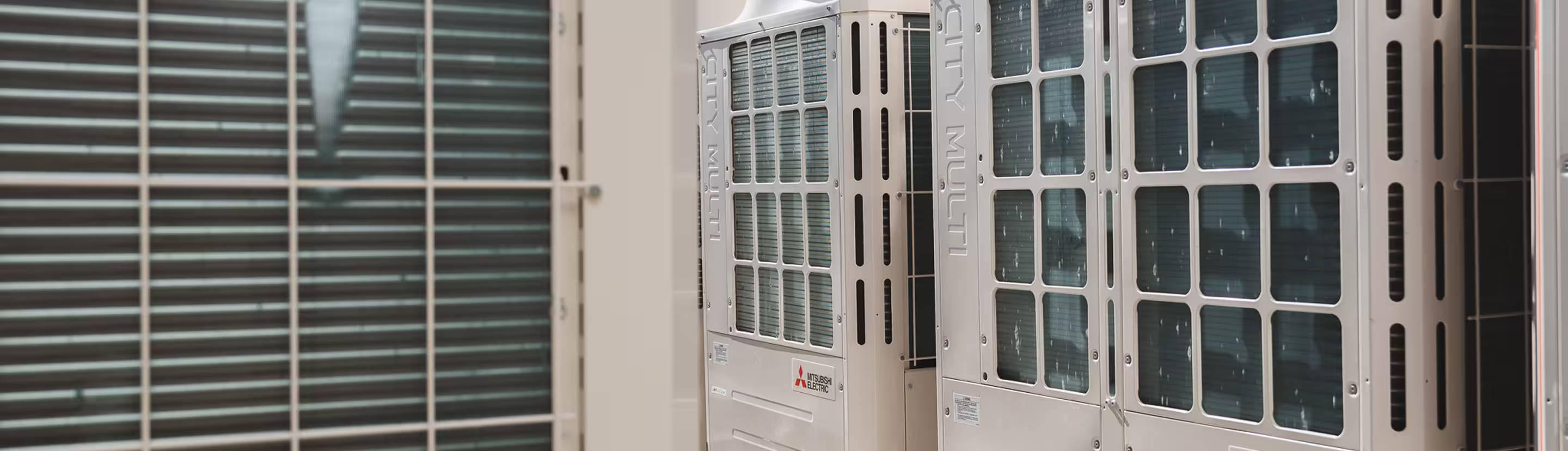 Close-up view of two Mitsubishi Electric City Multi outdoor air conditioning units mounted against a building wall.