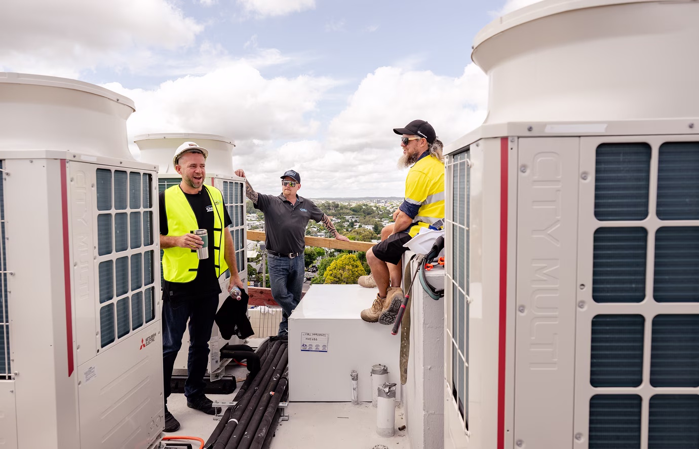 Three Chill Merchants team members standing among Mitsubishi Electric City Multi VRF condenser units on a commercial rooftop