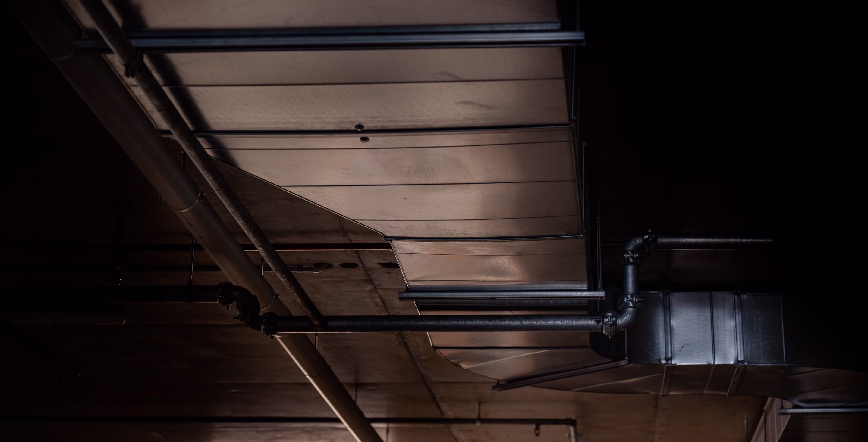 Metallic air ducts and pipes running across a dimly lit industrial ceiling.