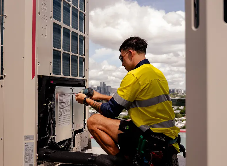Chill Merchants technician in hi-vis and sunglasses servicing the internal wiring of a Mitsubishi Electric condenser unit on a rooftop