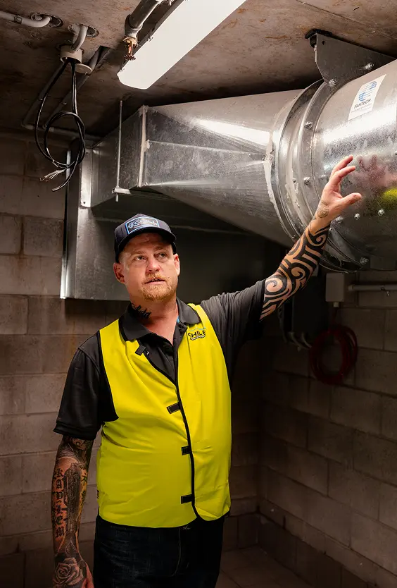 Chill Merchants technician in hi-vis and cap inspecting galvanised ductwork in a commercial ceiling space
