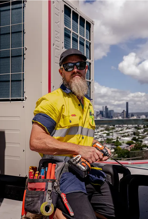 Senior Chill Merchants technician in hi-vis with tool belt servicing a rooftop condenser unit with Brisbane skyline behind