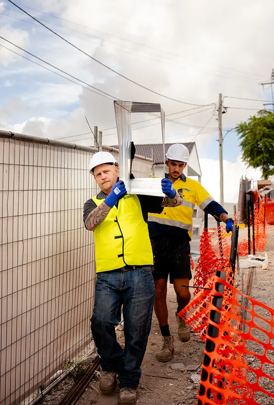 Two Chill Merchants technicians in hi-vis carrying equipment through a fenced construction site