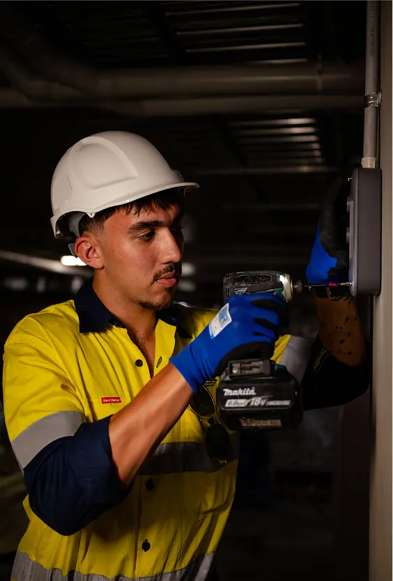 Chill Merchants HVAC technician in hi-vis and hard hat using a Makita cordless drill in a commercial plant room