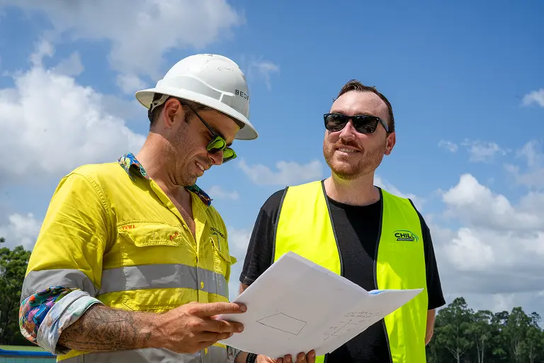 Two Chill Merchants team members in hi-vis reviewing project plans together on a rooftop on a sunny day