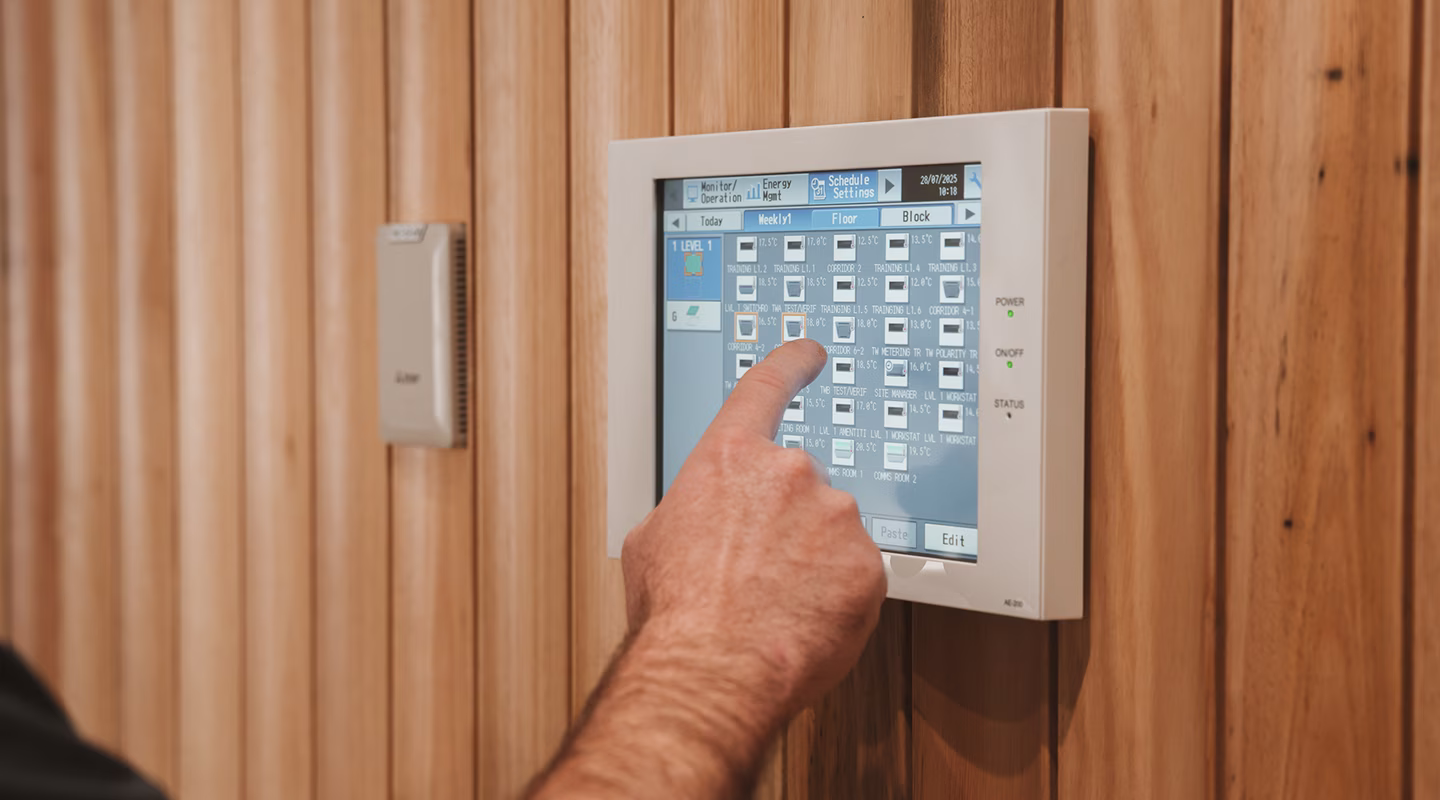 Wall-mounted HVAC zone controller touchscreen panel being operated by hand