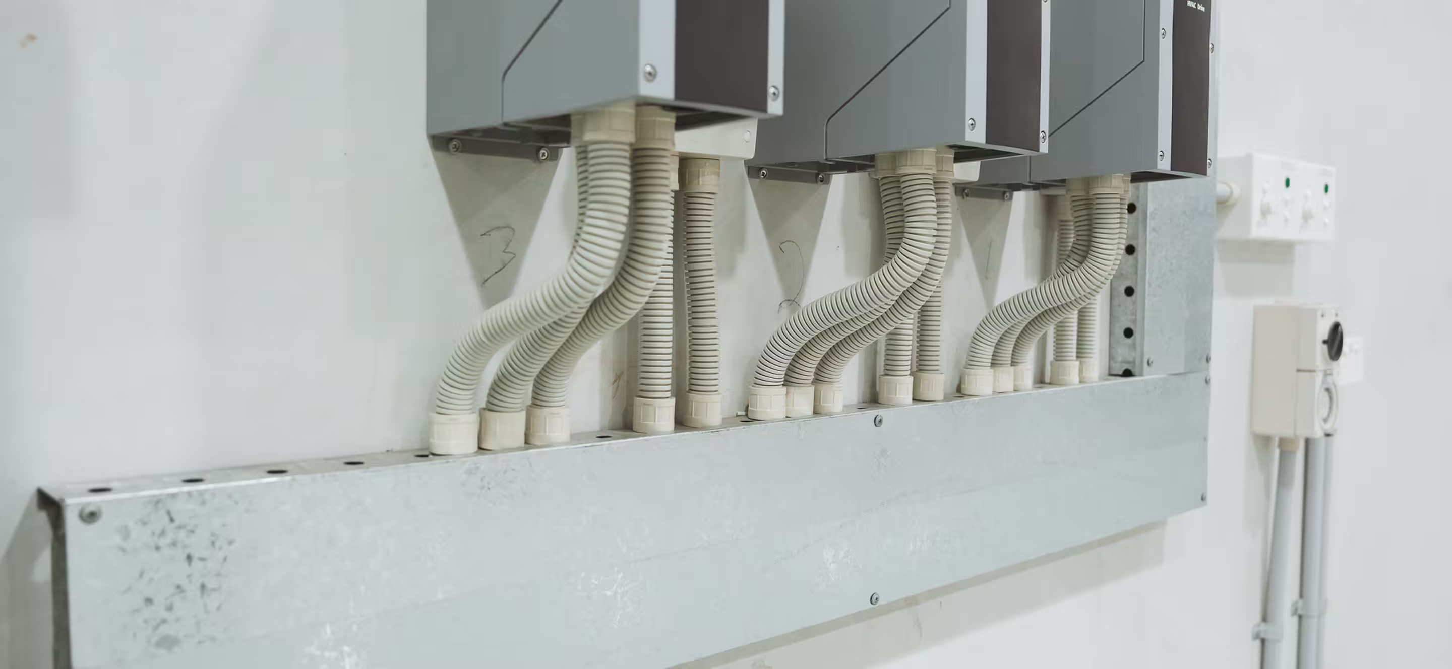 Electrical conduit pipes connected to industrial control boxes mounted on a white wall.