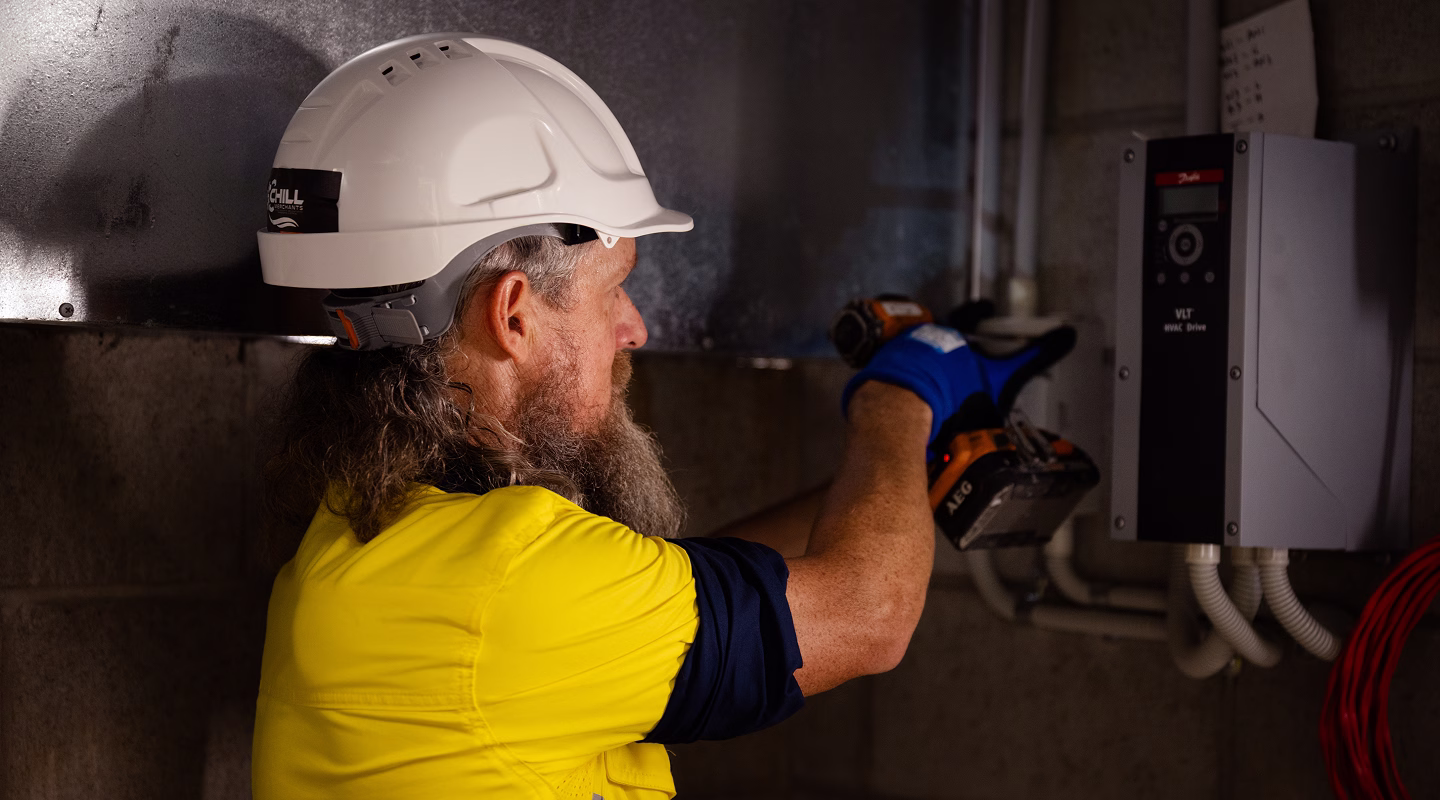A technician in a hard hat inspecting an electrical switchboard for compliance