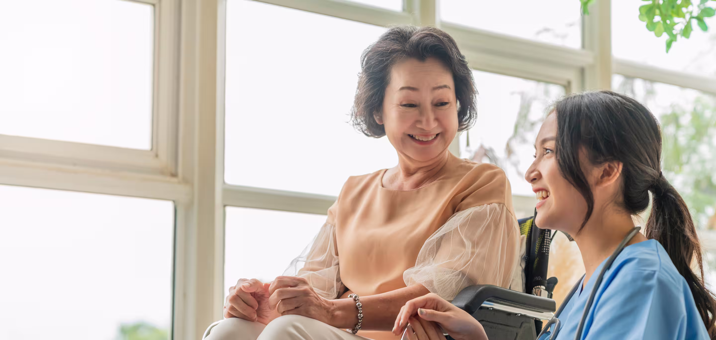 Elderly resident smiling with a younger carer in a comfortable, climate-controlled aged care facility environment