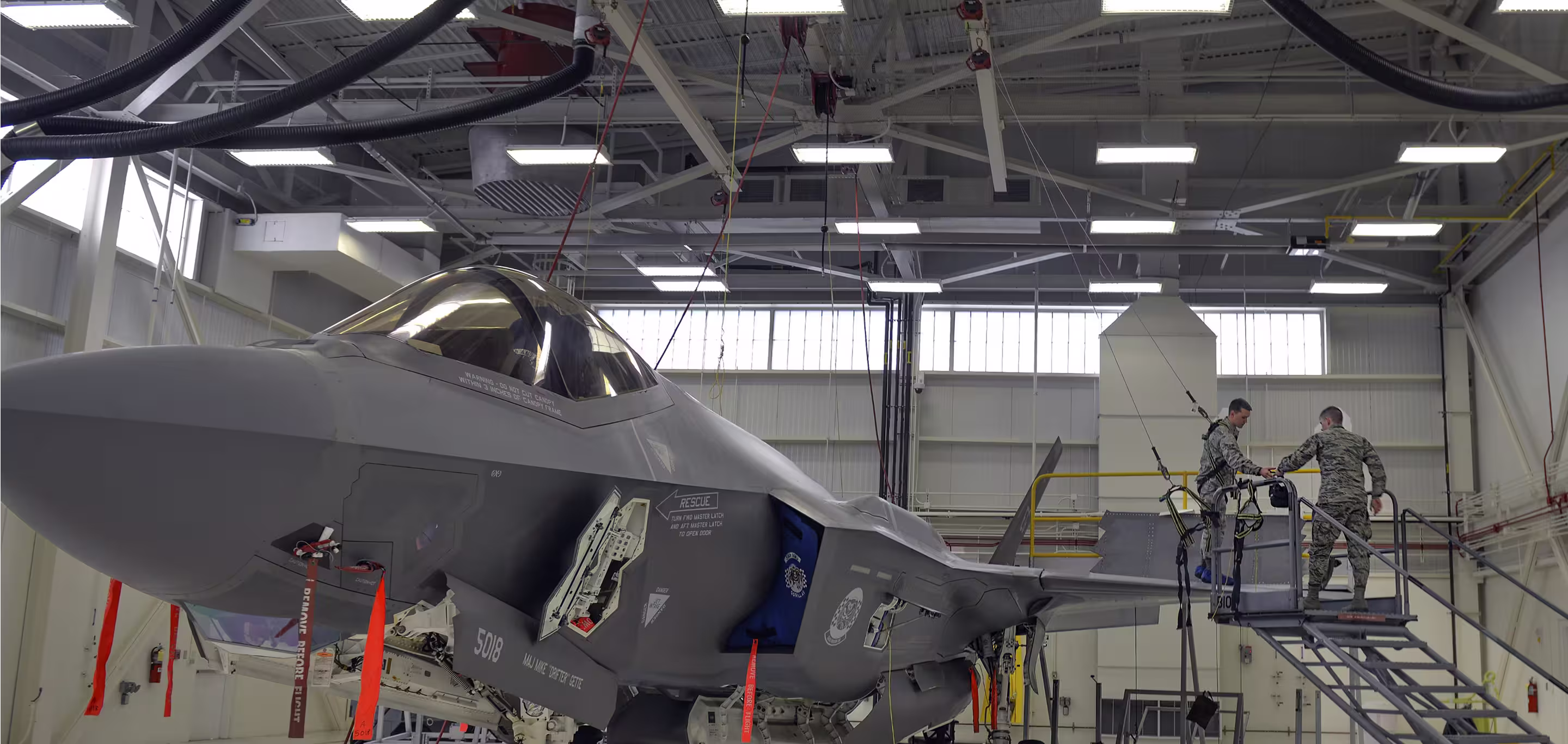 Military aircraft inside a large climate-controlled defence hangar facility with personnel performing maintenance under HVAC-regulated conditions