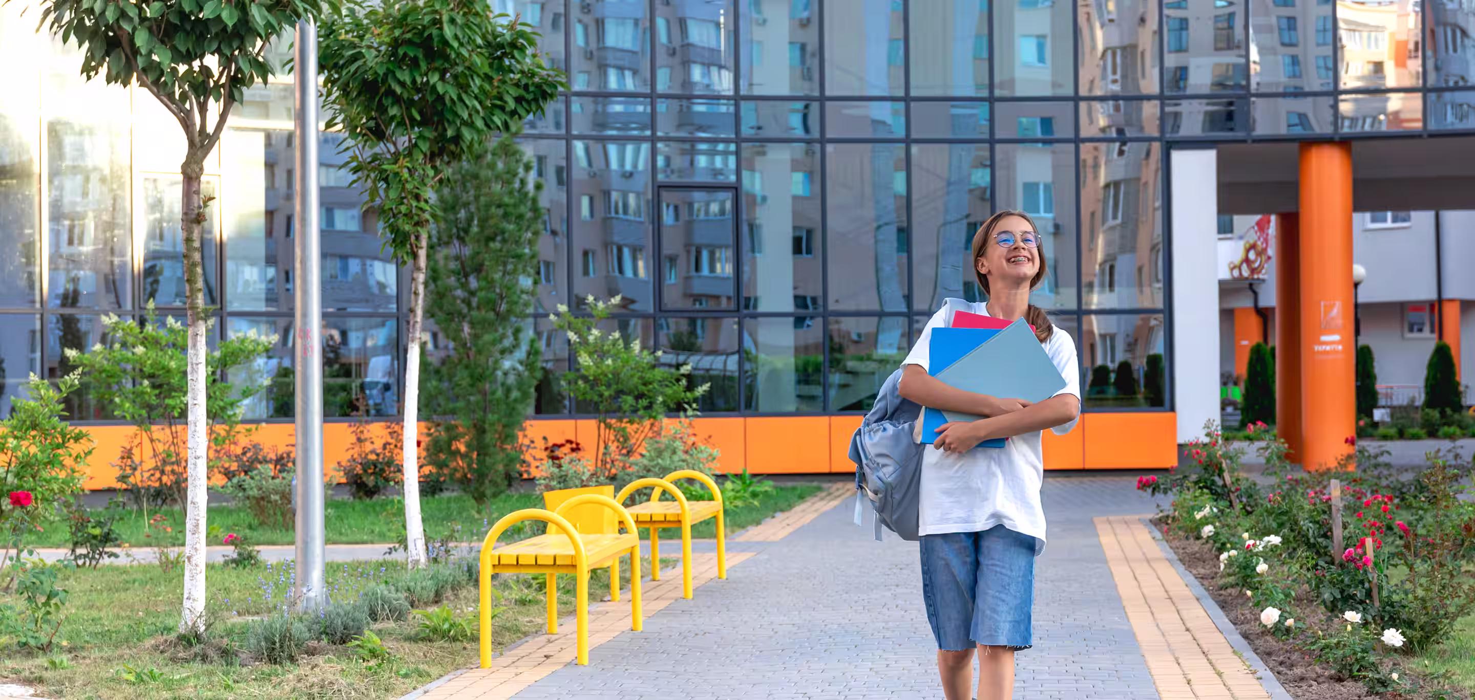 Student carrying folders walking through a modern school campus courtyard to represent HVAC services for education facilities