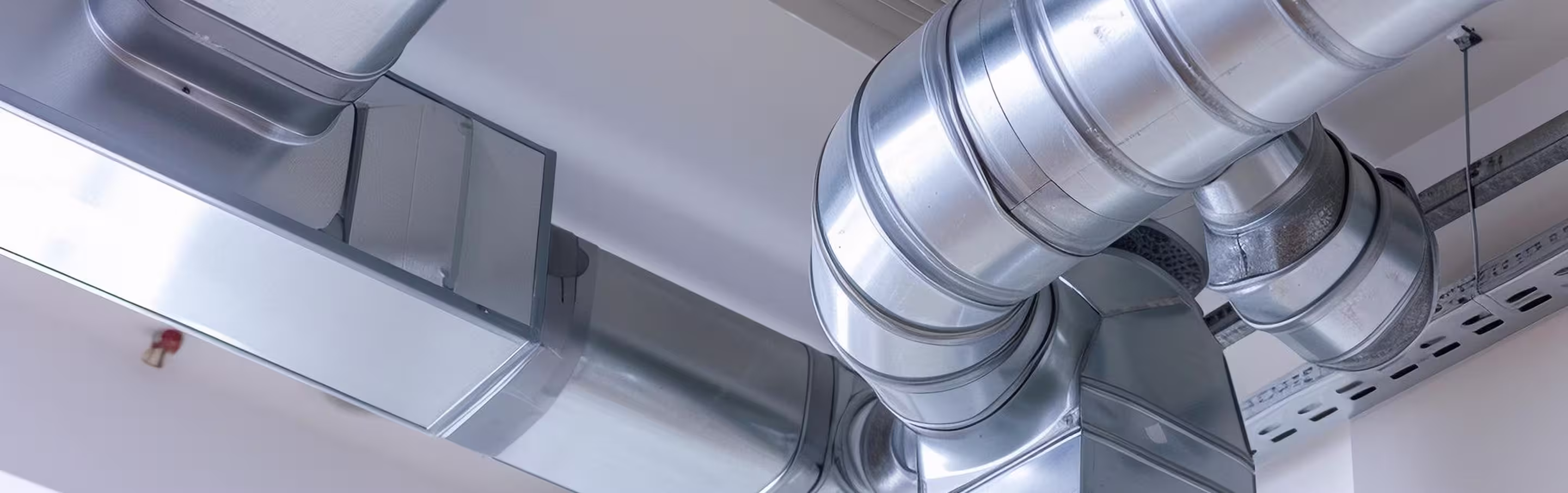Close-up view of shiny metal HVAC ductwork and ventilation pipes on a ceiling.