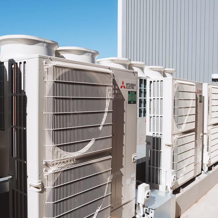 Row of Mitsubishi Electric outdoor air conditioning units installed on a concrete platform under clear blue sky.