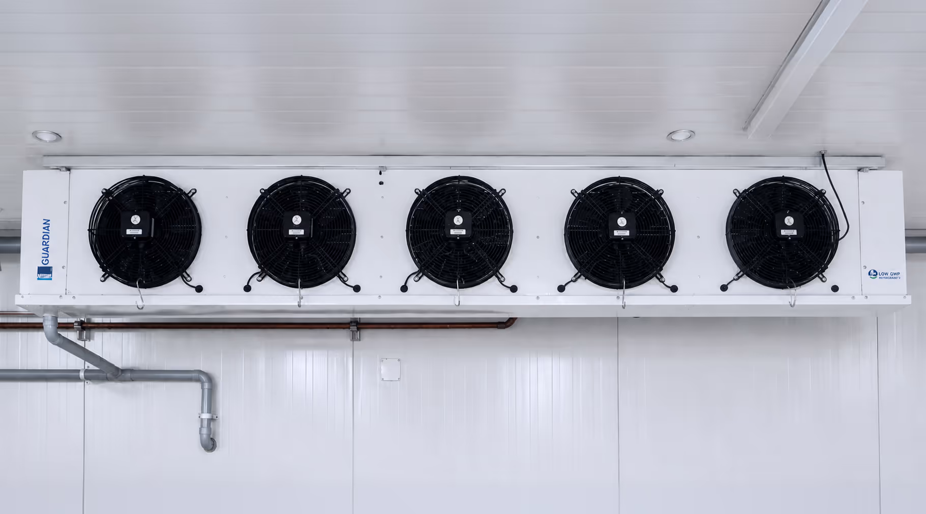 Industrial air conditioning unit mounted on a white wall with five black fans in a row inside a clean facility.