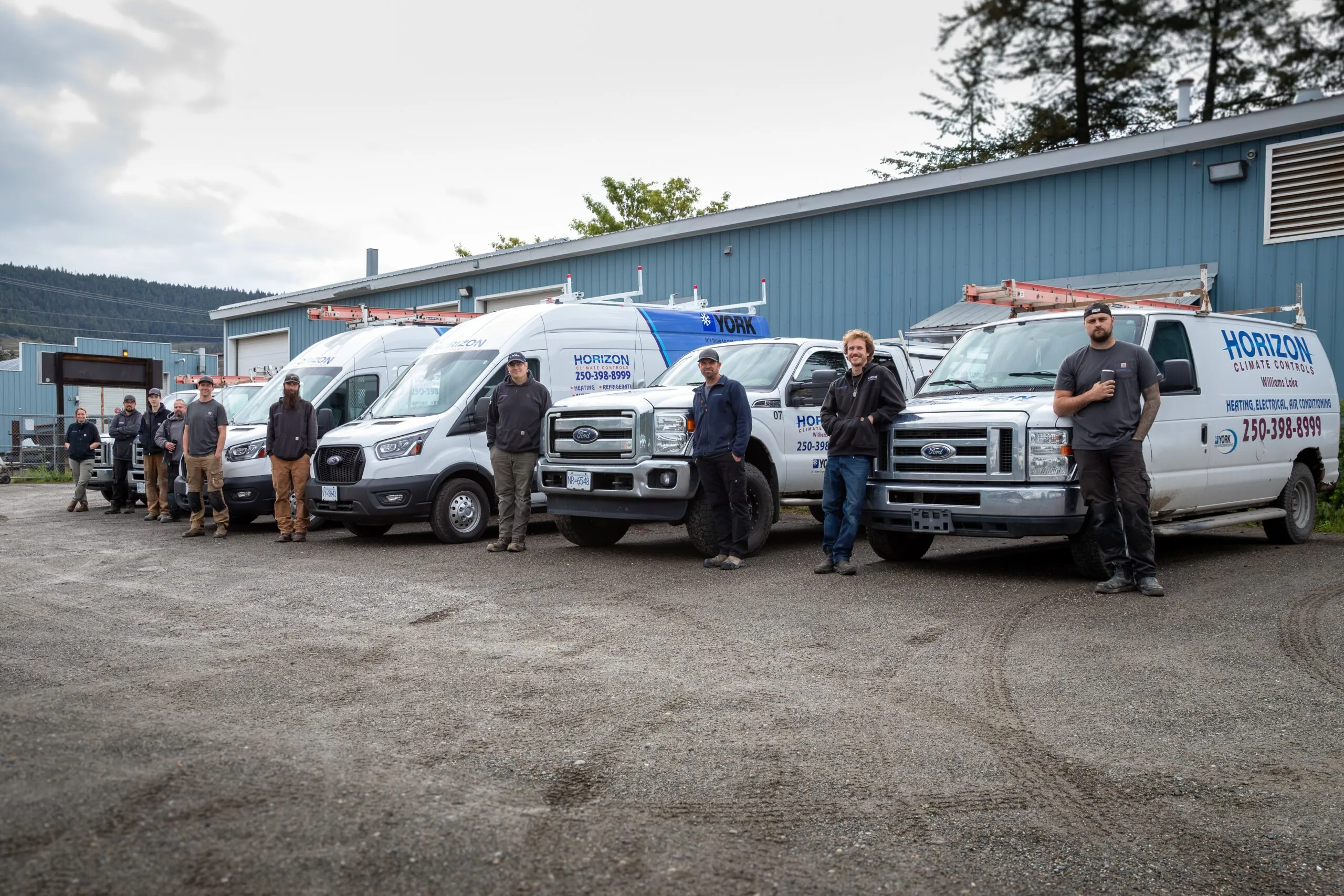 A line of workers stands beside branded Horizon Climate Controls vans outside a blue industrial building.