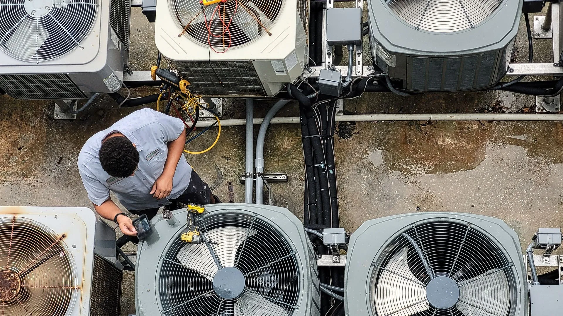 Technician inspecting and cleaning a rooftop air conditioning unit among several HVAC units.