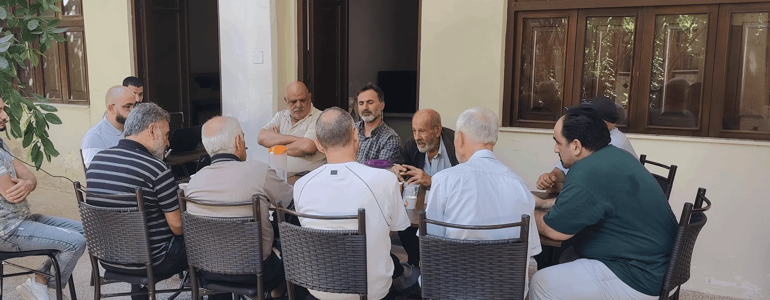 A group of people seated around a table in what appears to be a meeting or roundtable discussion in an indoor setting with ornate architectural details.