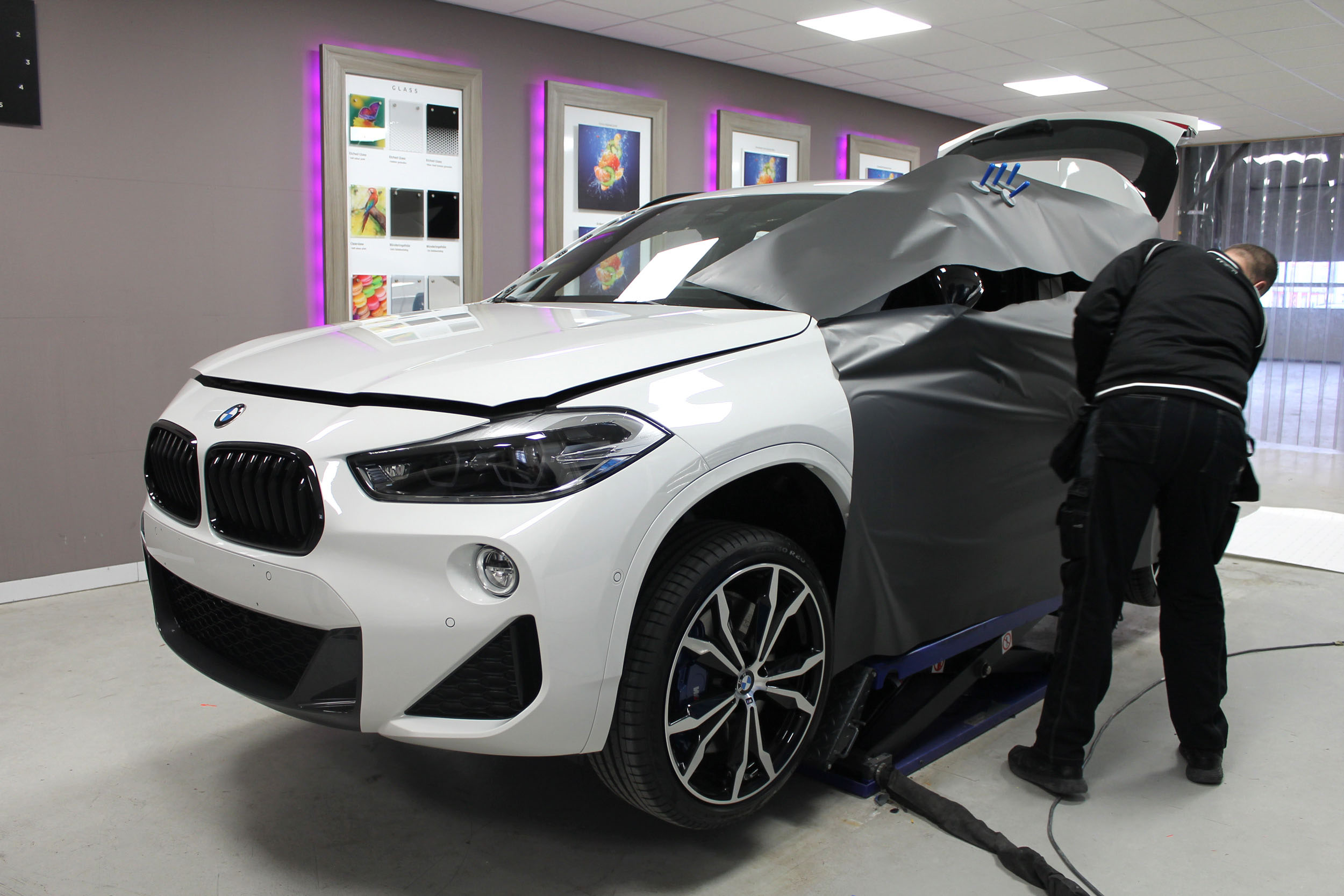 Iemand brengt een grijze vinylfolie aan op de zijkant van een witte BMW SUV in een garage.