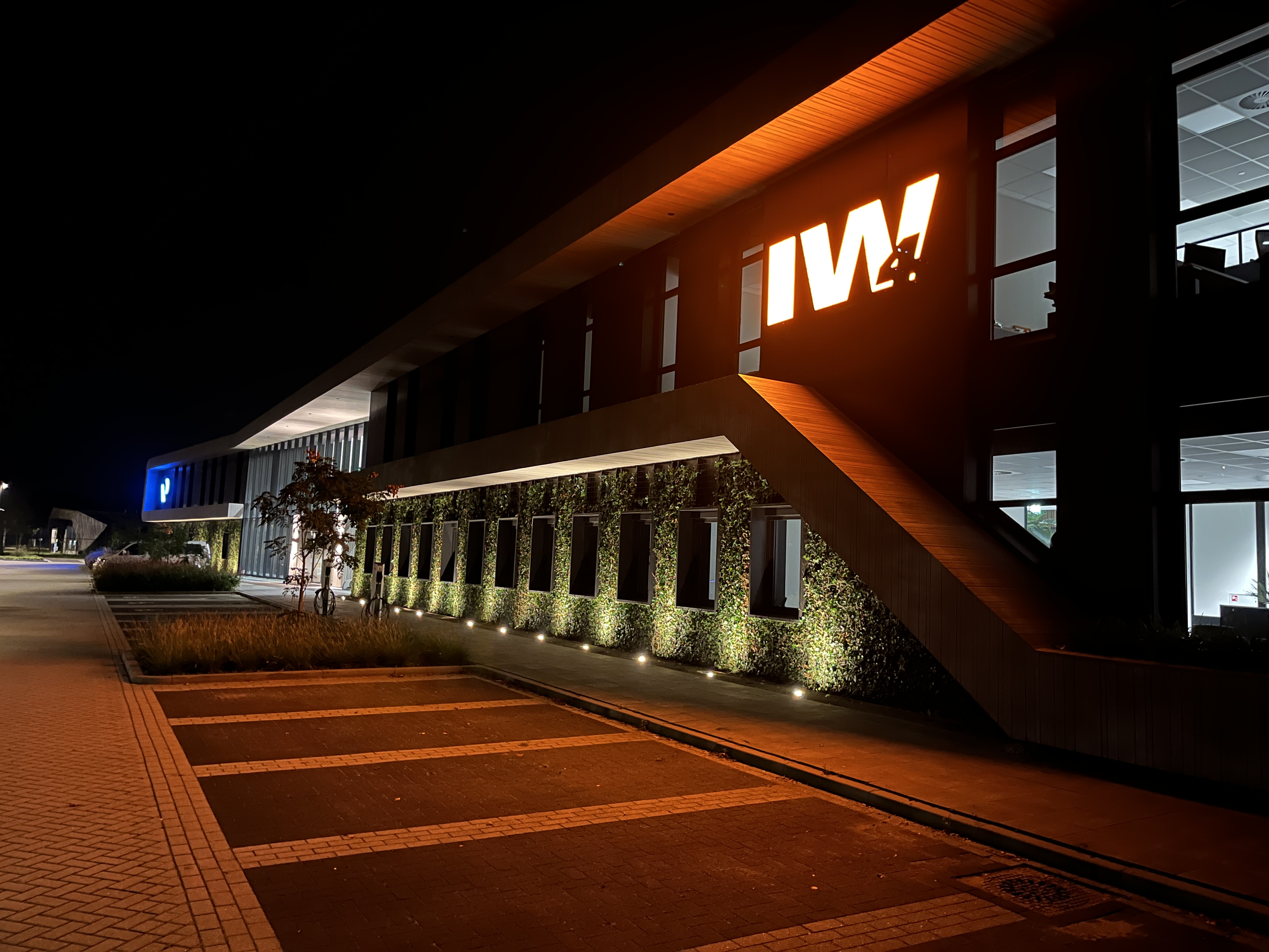 Modern kantoorgebouw verlicht in de nacht met opvallend oranje en blauw neonlogo's.