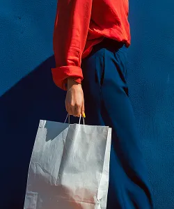 Person holding a silver shopping bag against a blue background