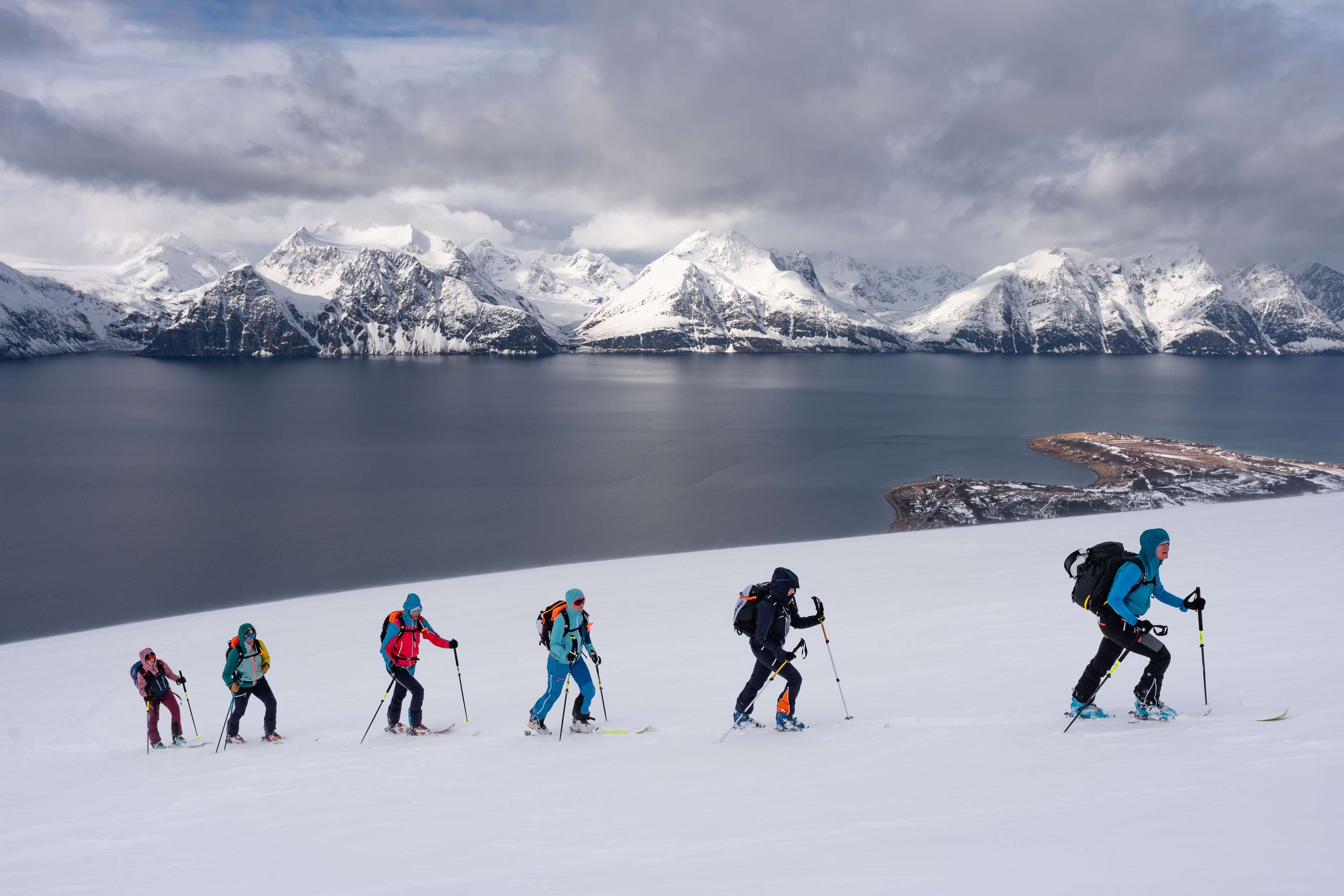 Skialpinisté na hřebeni nad temným fjordem