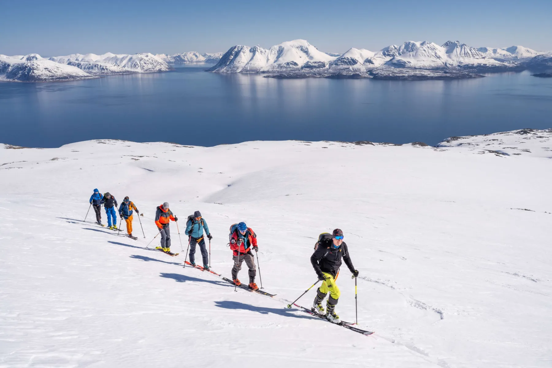 Skupina na skialpech stoupá s výhledem na fjord