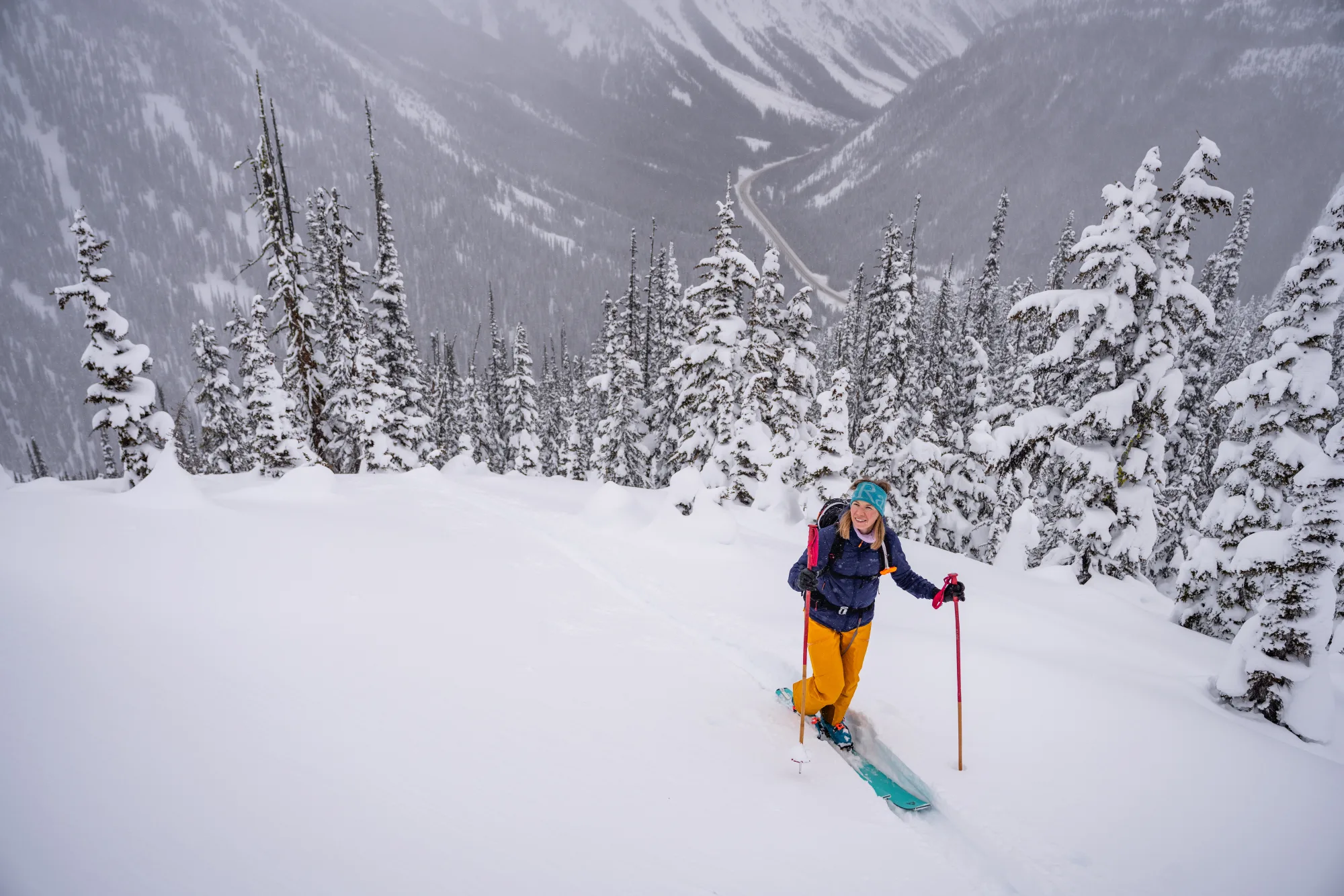 Skialpinistka stoupá vysoko nad Trans-Canada Highway, Rogers Pass
