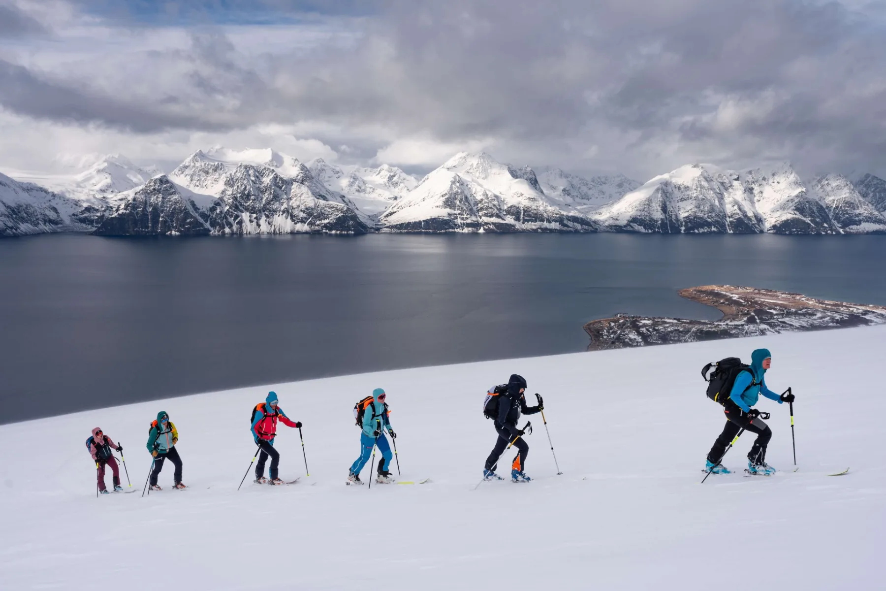 Skialpinisté na hřebeni nad temným fjordem