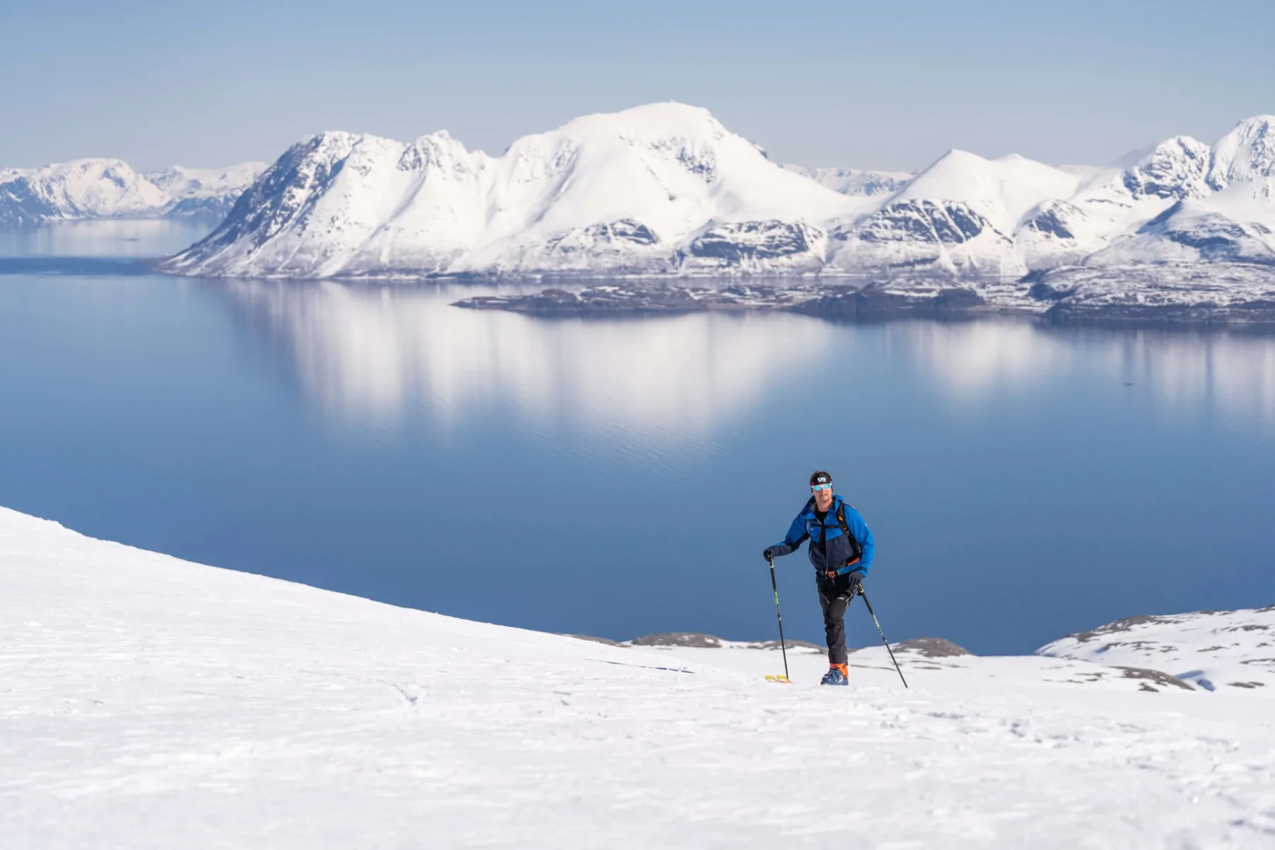 Skialpinista nad zrcadlově klidným fjordem, Norsko