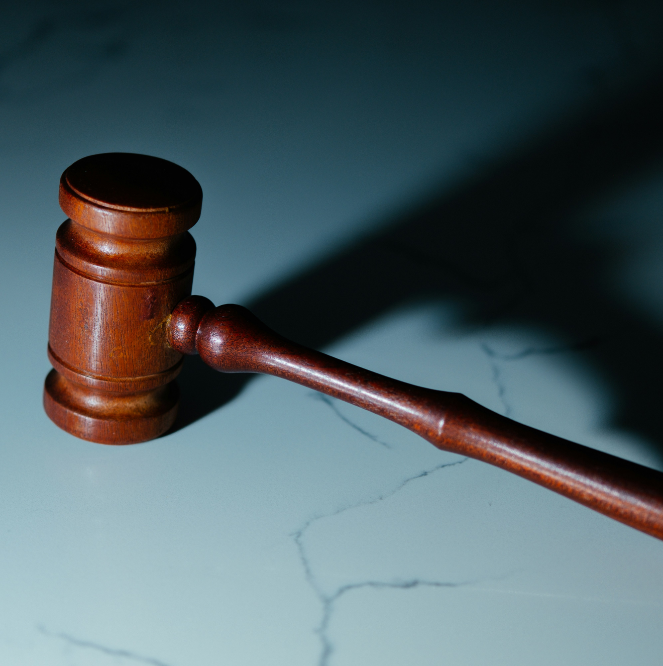 Wooden judge's gavel resting on a gray marble surface casting a shadow.