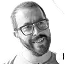 Smiling man with glasses and a beard wearing a gray shirt.