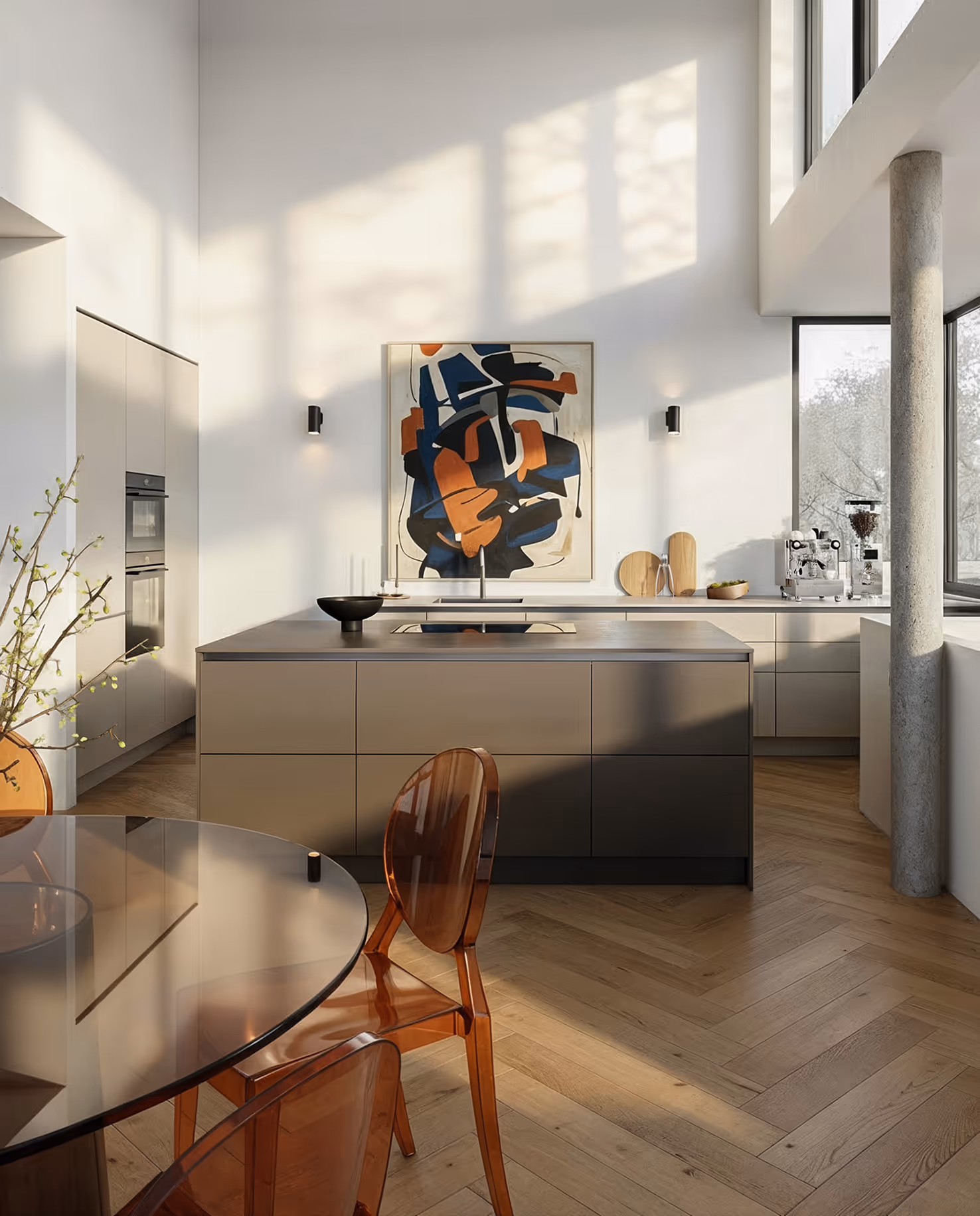 Moderne Küche mit Kücheninsel, großen Fenstern, abstractem Wandbild und transparenten braunen Stühlen um runden Glastisch.