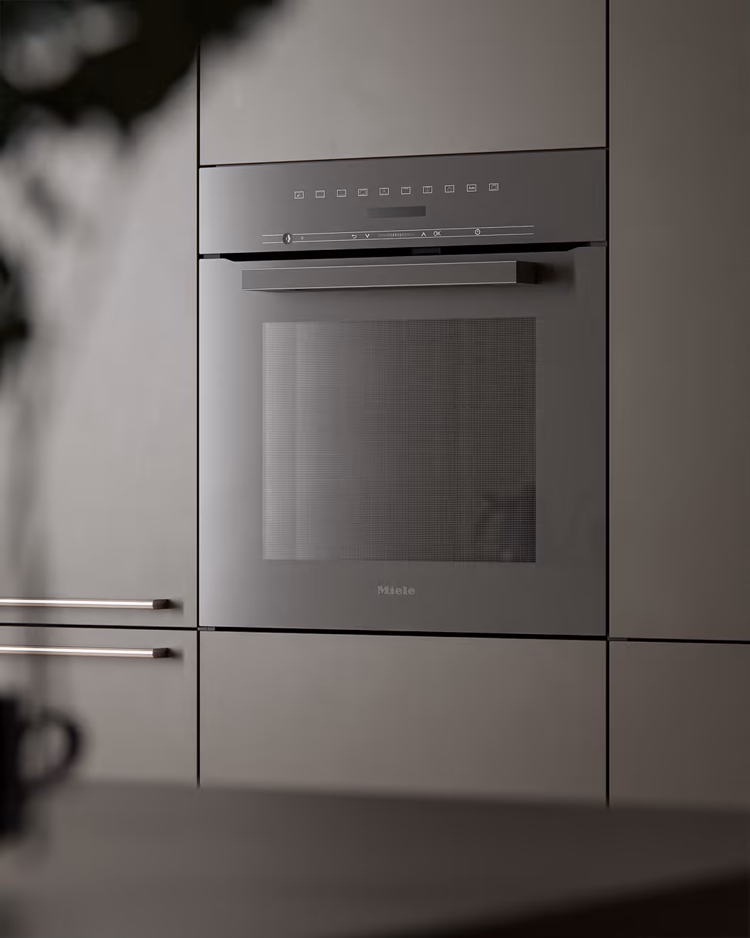 Ein eingebauter grauer Miele-Backofen in einer modernen, hellen Küchenzeile.