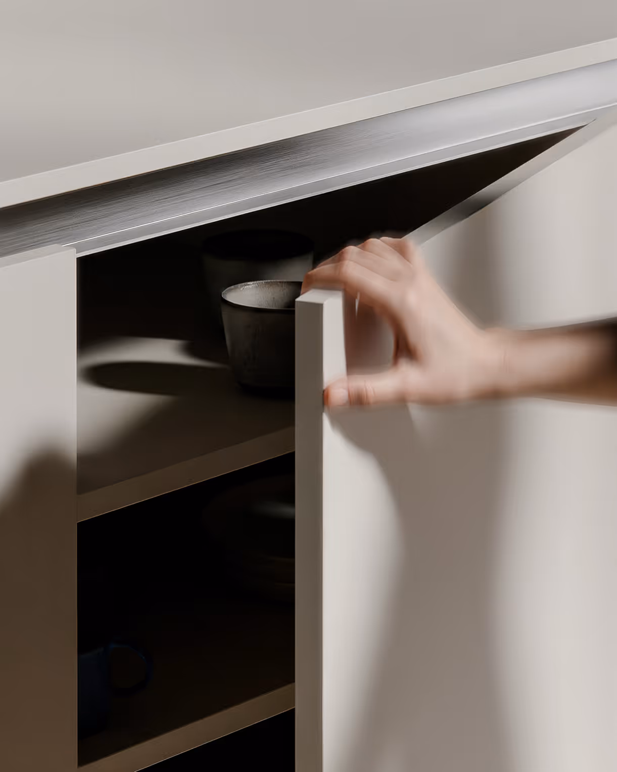 Eine Hand öffnet einen weißen Küchenschrank mit Keramiktassen und -tellern im Inneren.
