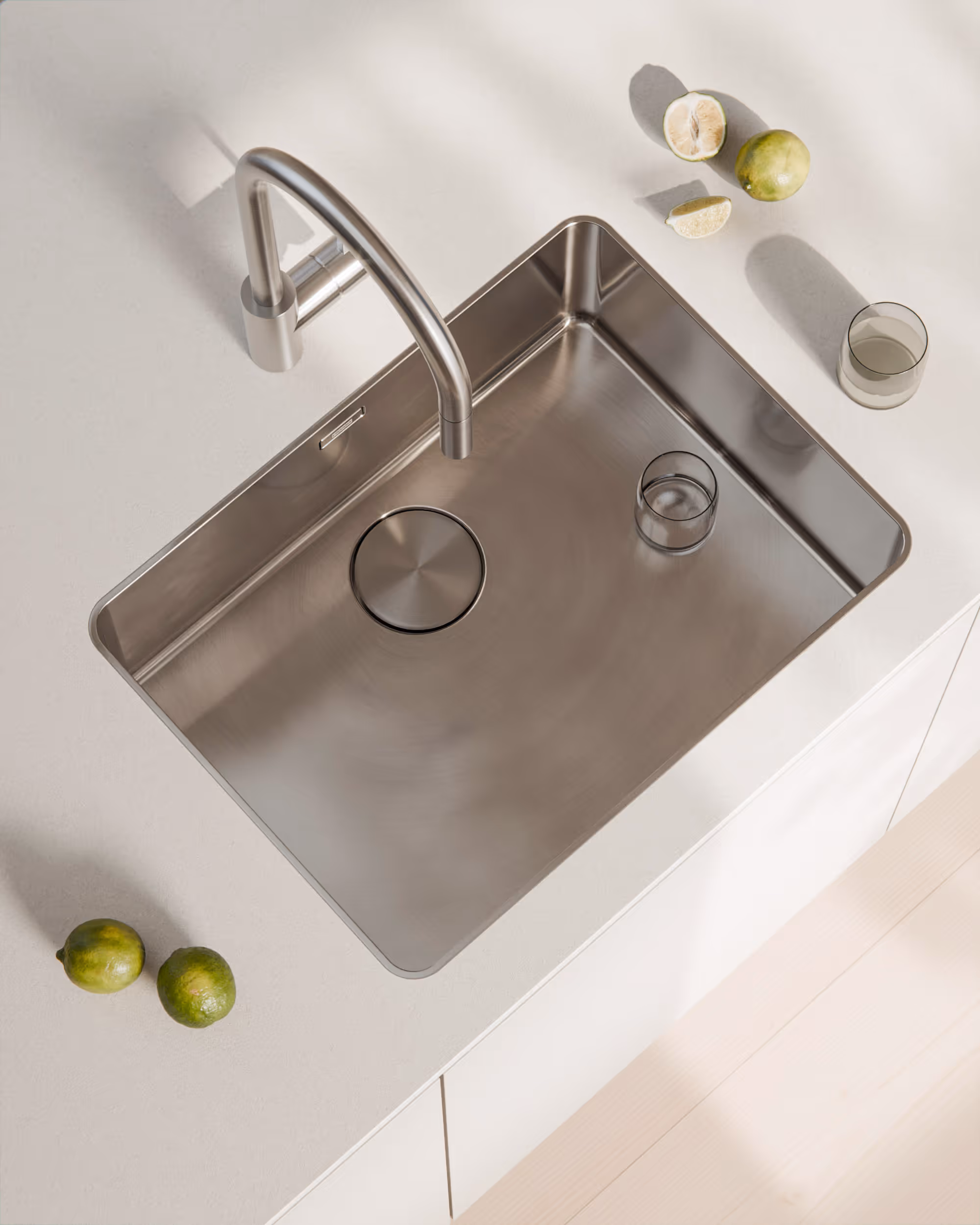 Moderner quadratischer Edelstahlspülbecken mit Armatur auf weißer Küchenarbeitsfläche und Limetten.