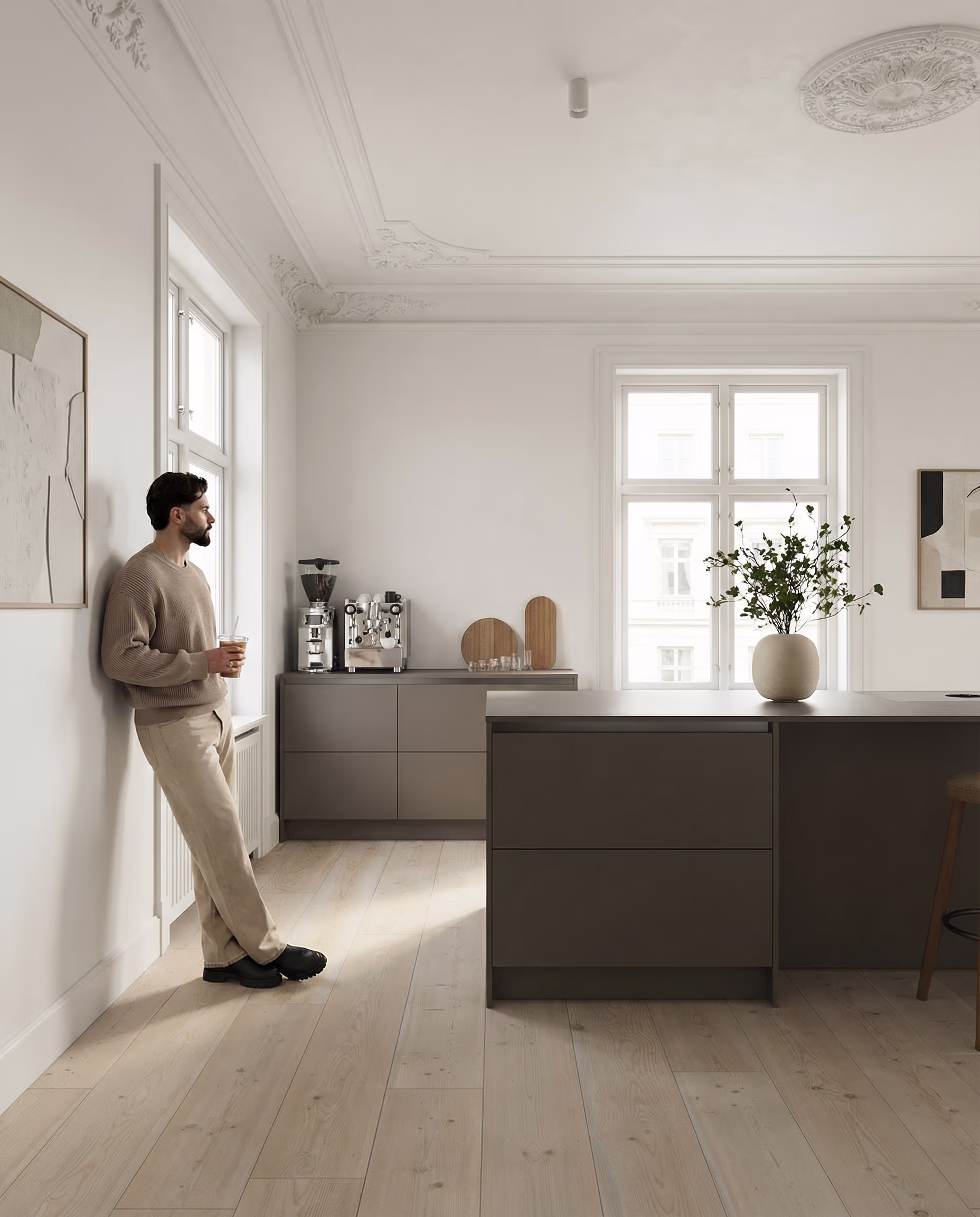 Mann lehnt an Wand in heller Küche mit Insel, Kaffeemaschine und Pflanzenvase.