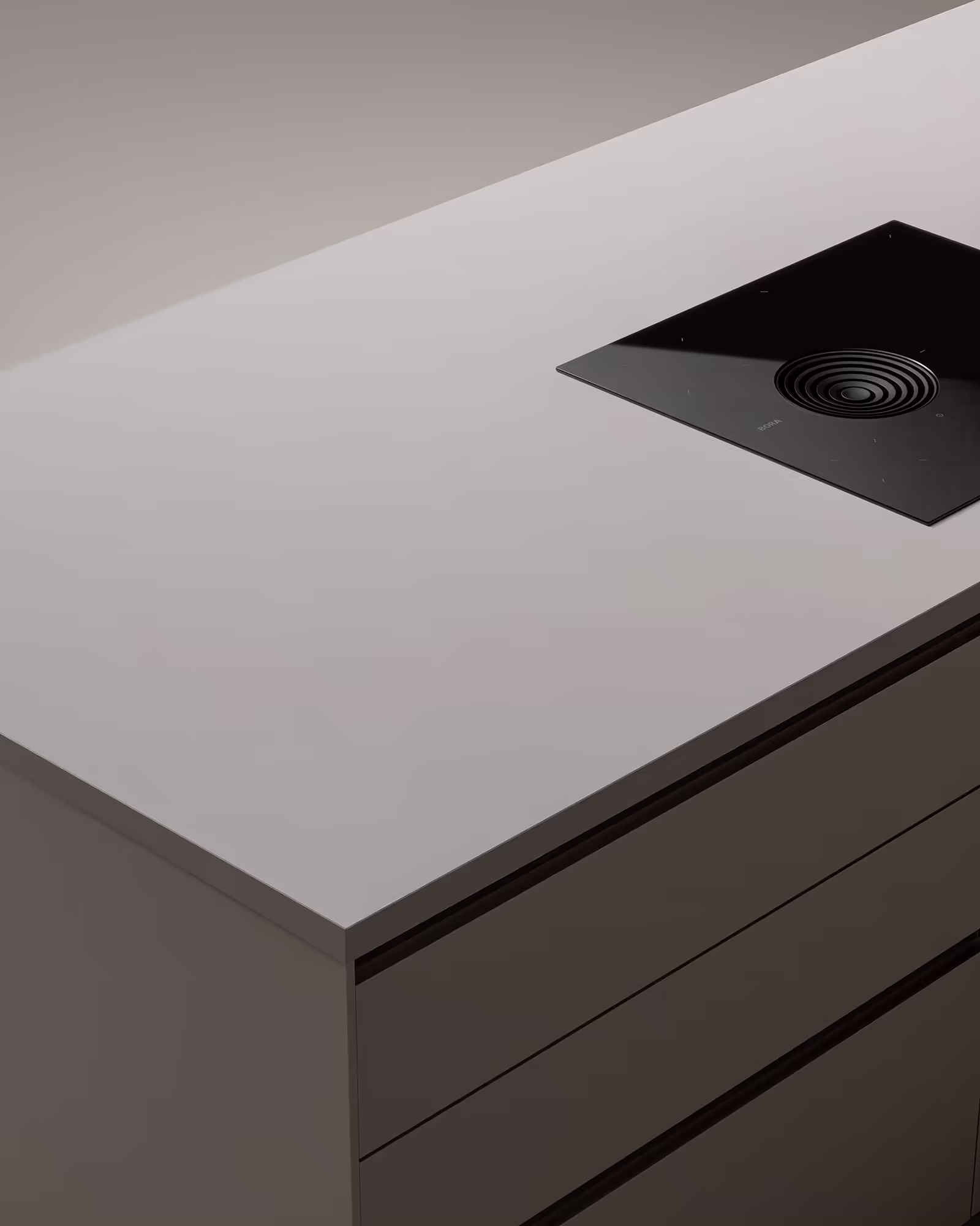Minimalistische Küchenarbeitsplatte mit mattem, grauem Oberflächenmaterial und einem schwarzen, integrierten Kochfeld mit zentraler Abluftöffnung.