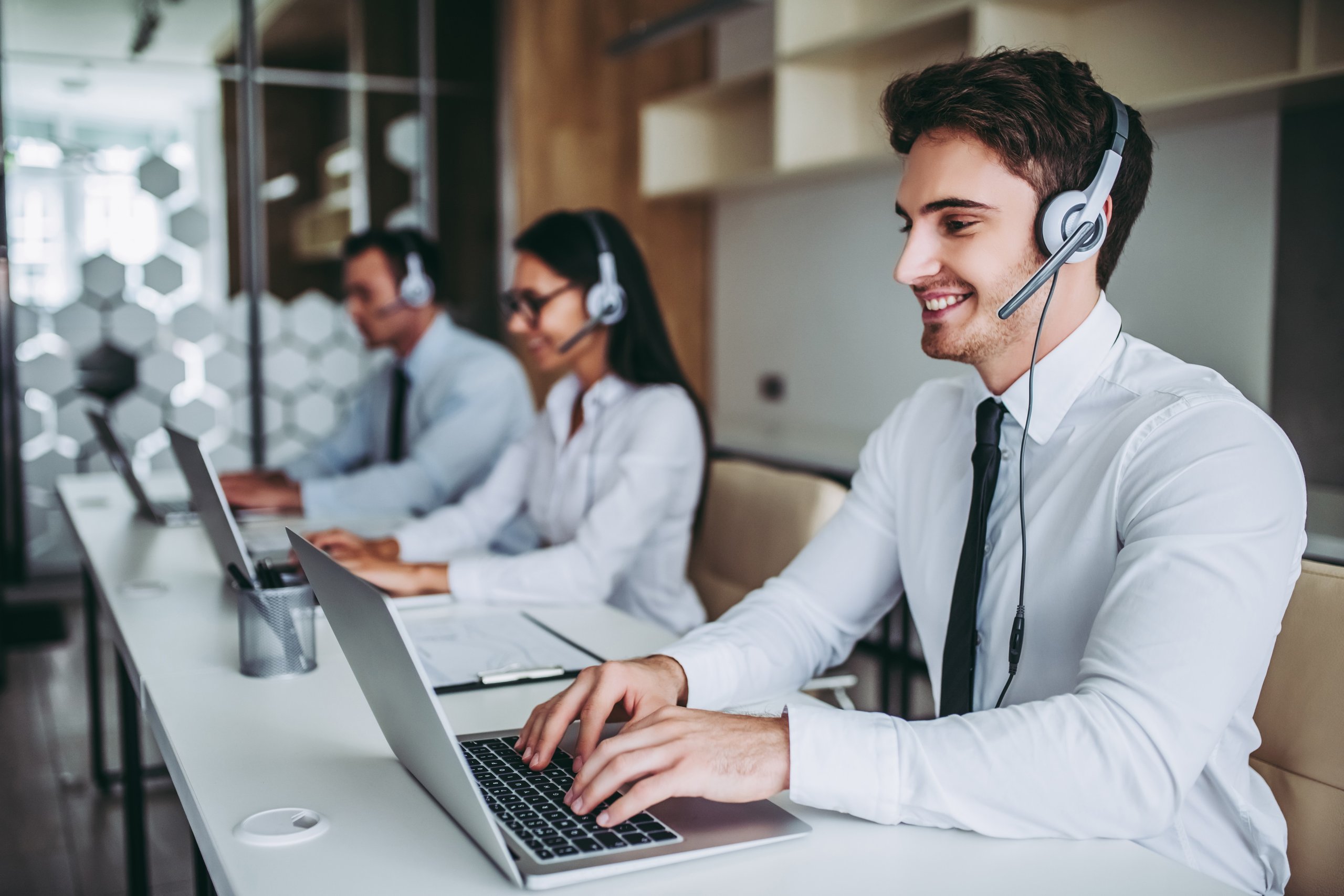 Three customer service representatives wearing headsets and working on laptops in a modern office.