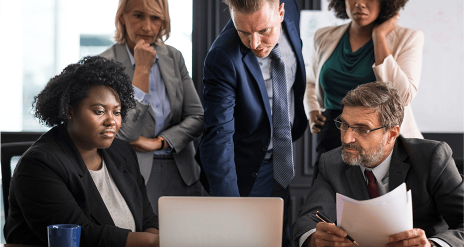 Group of five business professionals focused on a laptop during a meeting in an office.