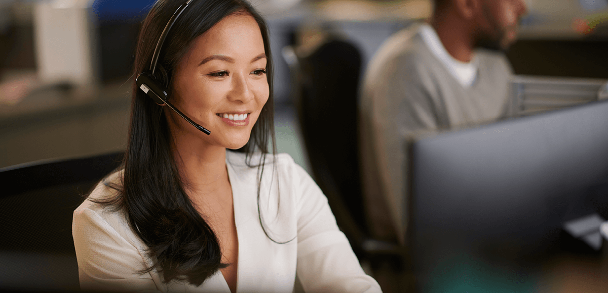 Smiling woman wearing headset working at a computer in a modern office.