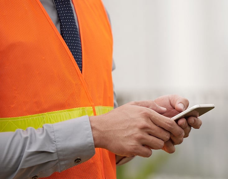 Man wearing an orange safety vest and blue tie using a smartphone.