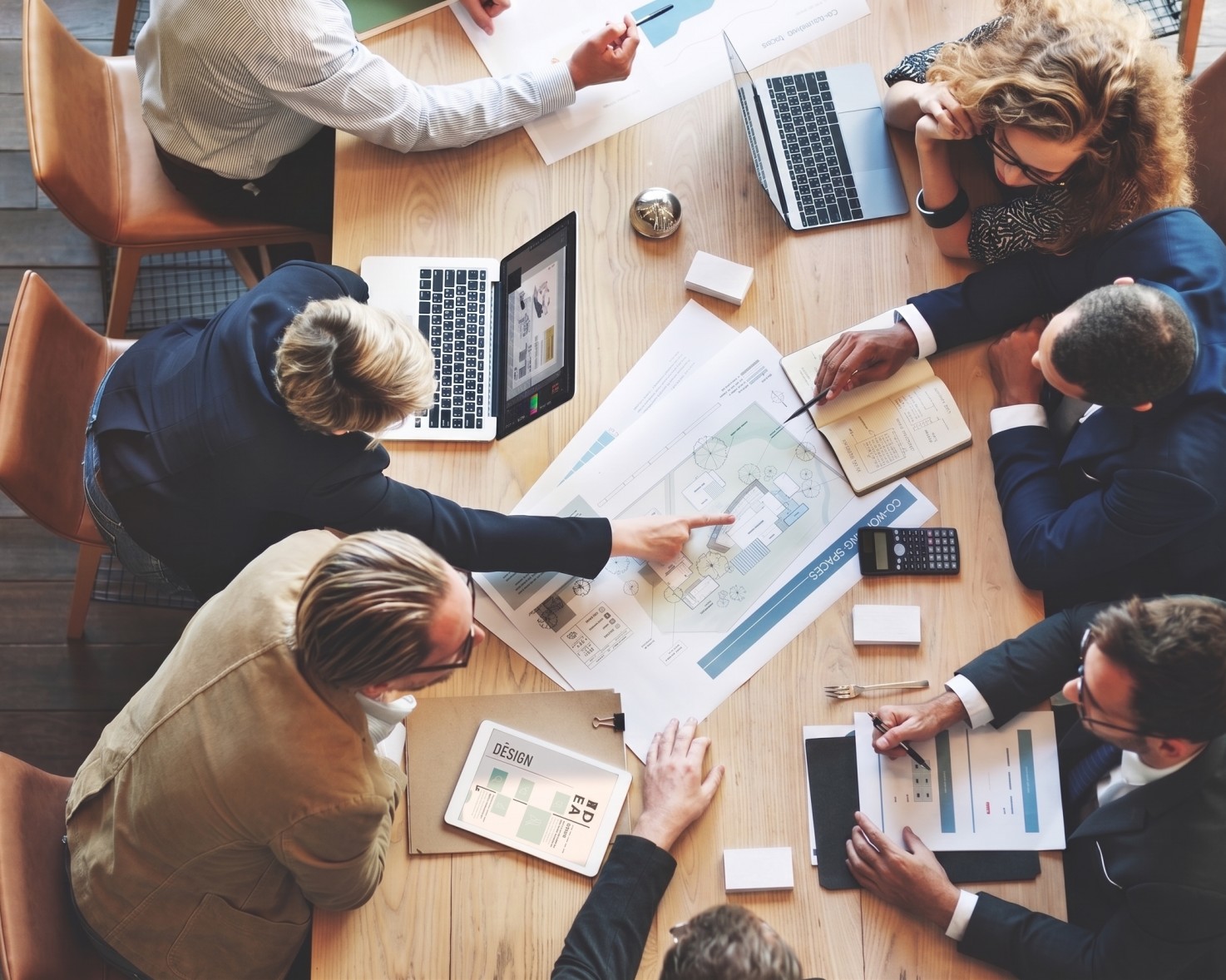 Overhead view of six professionals collaborating around a table with laptops, architectural plans, and documents.