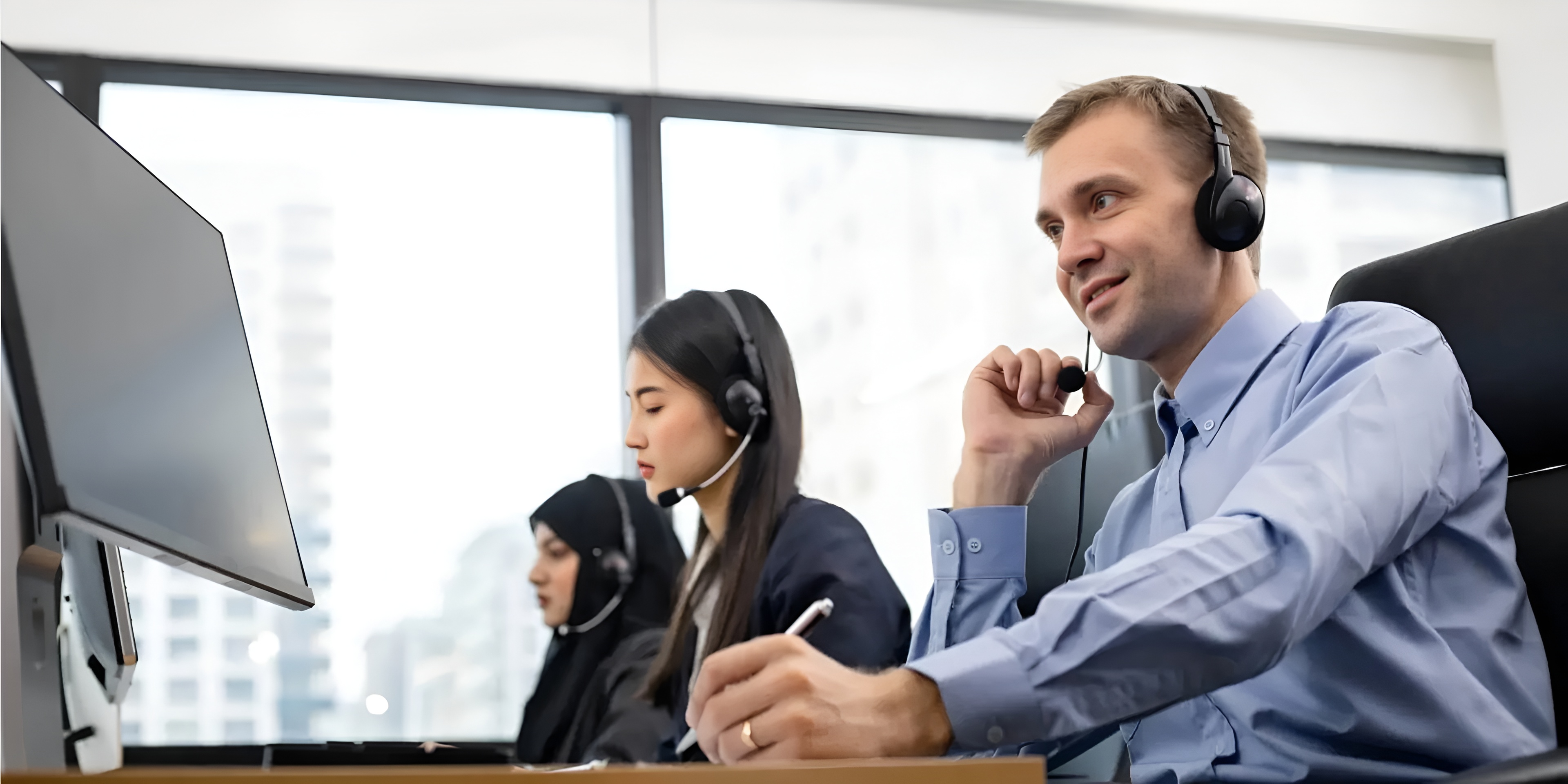 Three customer service representatives wearing headsets working at desks with computers in an office.