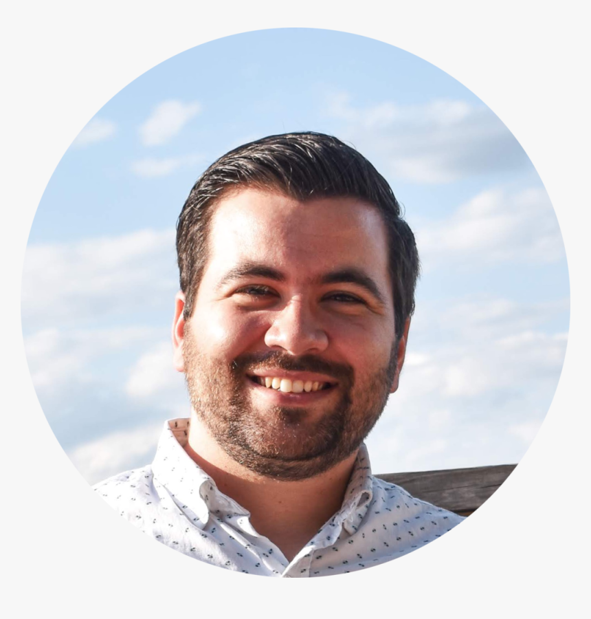 Smiling man with short dark hair and a beard wearing a white shirt with small patterns under a partly cloudy sky.