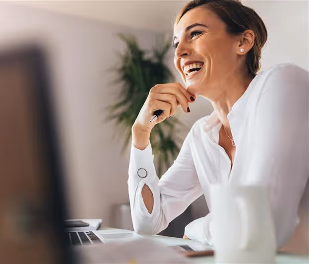 Donna sorridente mentre lavora al computer in un ambiente d'ufficio luminoso.