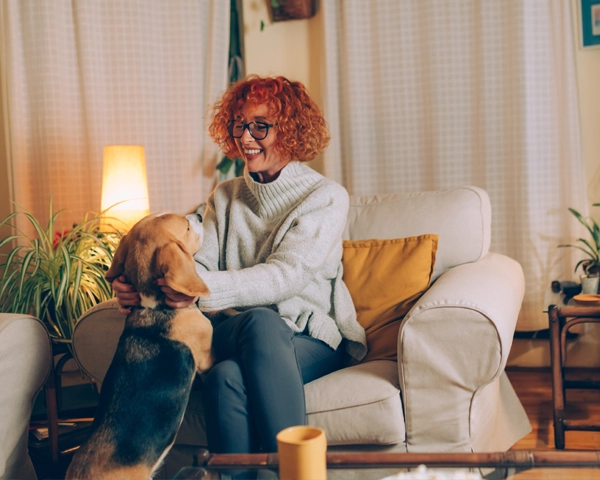 Eine Frau mit roten Locken sitzt auf einem Sessel und streichelt ihren Beagle, der mit den Vorderbeinen auf ihrem Bein steht.
