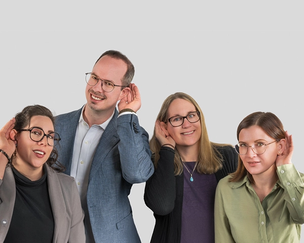 Das Team von Hörtechnik Hauser steht nebeneinander und lächelt in die Kamera. Jeder hat eine Hand hinters Ohr gelegt.