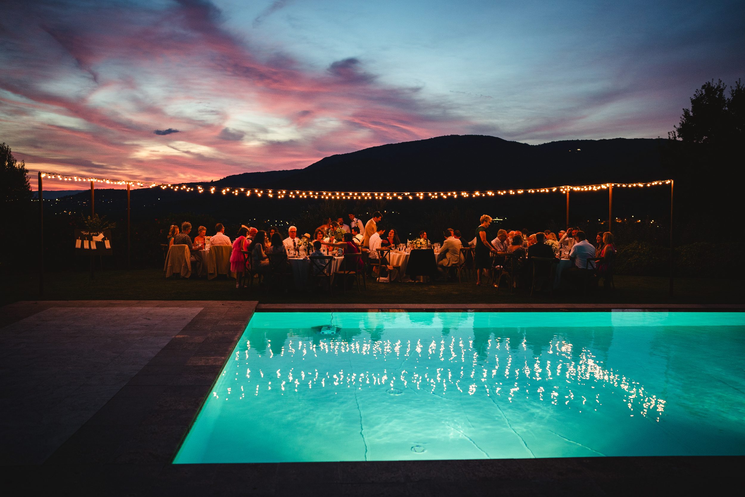 Sunset over the pool at a Tuscany wellness retreat with string lights and a long dinner table